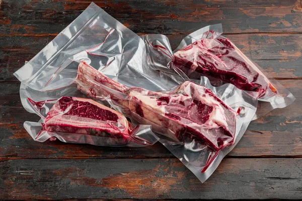 Dry aged steak in a vacuum marbled beef meat pack set, tomahawk, t bone and club steak cuts, on old dark  wooden table background