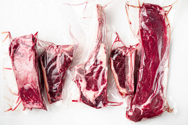 Beef steak vacuum set, tomahawk, t bone, club steak, rib eye and tenderloin cuts, on white stone  background, top view flat lay