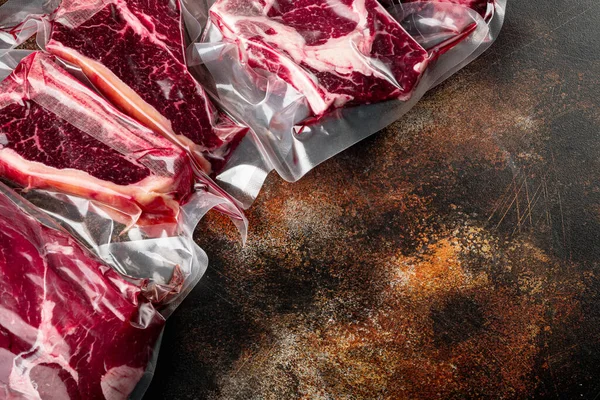 Beef steak vacuum sealed ready for sous vide cooking set, tomahawk, t bone, club steak, rib eye and tenderloin cuts, on old dark rustic background, with copy space for text