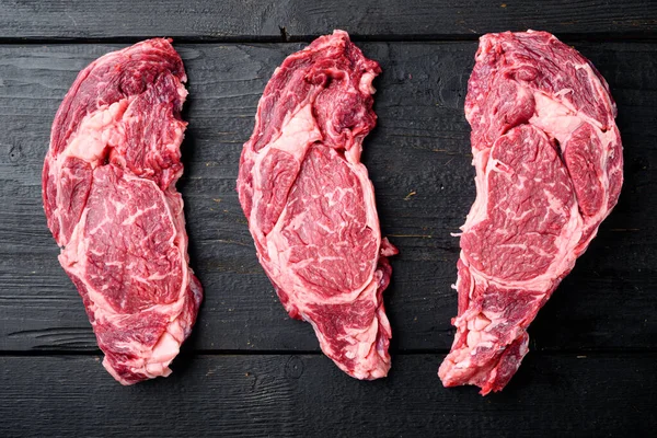 Black Angus prime beef rib eye steak, marbled meat set, on black wooden table background, top view flat lay