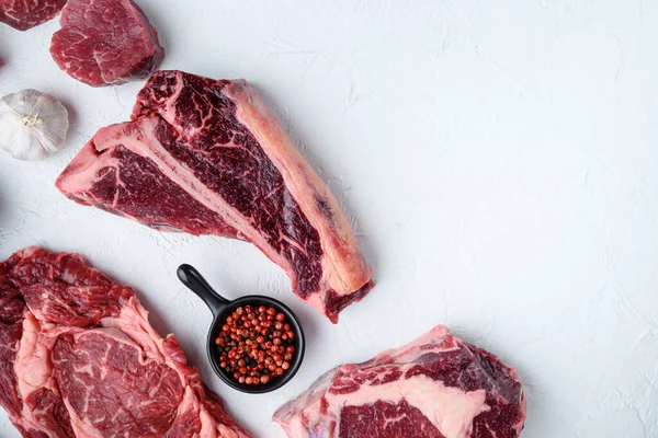 Various cuts of marbled beef meat and dry aged steaks set, tomahawk, t bone, club steak, rib eye and tenderloin cuts, on white stone  background, top view flat lay, with copy space for text