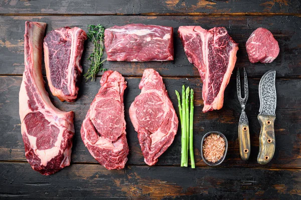 Çiğ Angus Prime et seti, tomahawk, t bone, sopa bifteği, pirzola ve fileto kesimi çeşitleri, eski koyu ahşap masa arka planında, üst görünüm düz yatıyordu