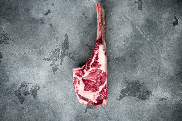 Raw uncooked black angus beef tomahawk steak on bone set, on gray stone background, top view flat lay, with copy space for text