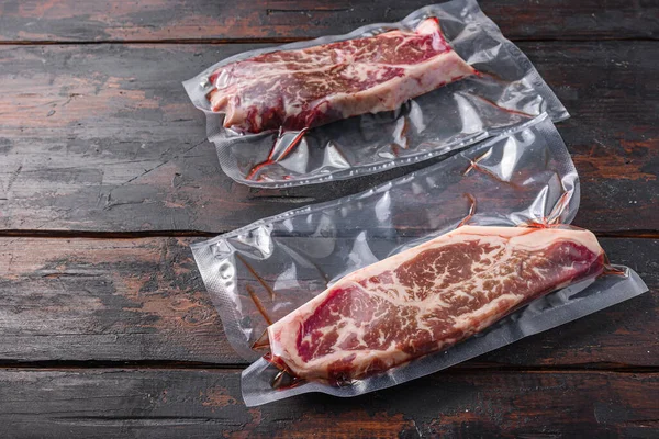 Vacuum packed meat , top blade beef steak on dark old wooden table,  side view space for text