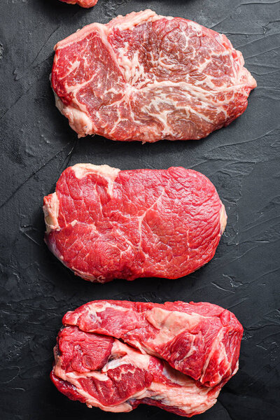 Raw set of rump, top blade, chuck roll beef steak cut, on black textured background, top view