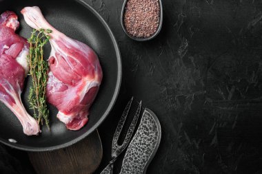 Çiftlik setinden yeni çıkmış organik çiğ ördek bacağı, kızgın dökme demir tavada, siyah taş zemin üzerinde, üst görünüm düz, kopyalanmış alan ve metin için boşluk