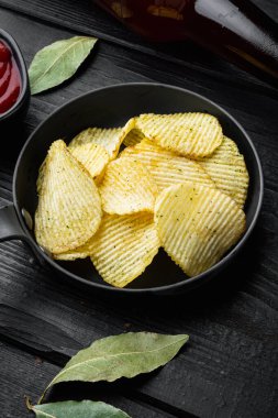 Çıtır patates cipsi. Patates dilimleri, deniz tuzu setiyle kızartılmış, siyah ahşap arka planda.