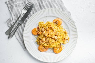 Deniz mahsullü erişteler, tabakta, beyaz taş yüzeyde, üst manzara düz.