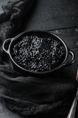 Siyah havyar kasesi, siyah ahşap masa arkasında.