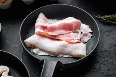 Cızırdayan pastırma parçaları dökme demir tavada, siyah arka planda.