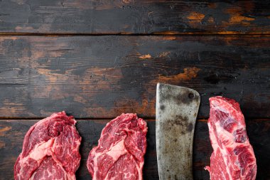 Taze çiğ Prime Angus bifteği seti, pirzola kesimi, eski koyu ahşap masa, üst görünüm düz, metin için kopyalama alanı ile
