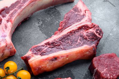 Gıda konsepti organik çiğ et seti, T kemik kesimi, gri taş arka planda.