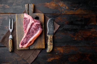 Barbekü seti için çiğ biftek, ahşap kesim tahtası, eski koyu ahşap masa arkaplanı, üst düz görünüm, metin için kopyalama alanı