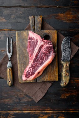 Çiğ mermer biftek seti, ahşap kesim tahtası, koyu ahşap arka plan, T kemik kesimi, üst manzara düz