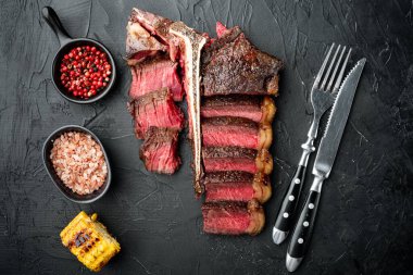Amerikan mutfağı. Dilimlenmiş ve rosto T-bone ya da biftek orta pişmiş az pişmiş biftek Biftek seti, siyah taş arka planda, üst manzara düz yatıyordu