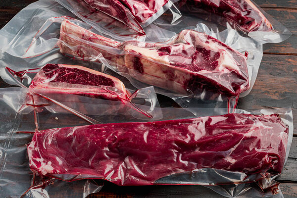 Raw beef meat in the vacuumed skin pack set, tomahawk, t bone, club steak, rib eye and tenderloin cuts, on old dark  wooden table background