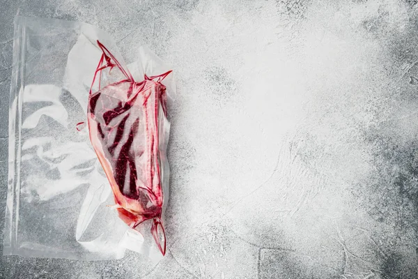 Fresh marbled meat black angus steak in vacuum plastic bag for sous vide set, on gray stone background, top view flat lay, with copy space for text