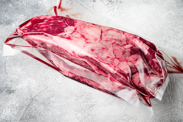 Fresh premium rib eye whole cut  in a vacuum pack package set, on gray stone background, with copy space for text