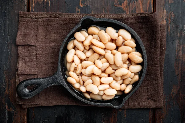 White canned beans set, in cast iron frying pan, on old dark  wooden table background, top view flat lay