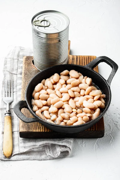 White canned beans set, with metal can, in cast iron frying pan, on white stone  surface