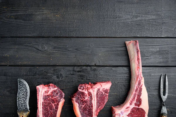 Various cuts of meat dry aged beef set, tomahawk, t bone or porterhouse and club steak, on black wooden table background, top view flat lay, with copy space for text