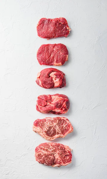 Rraw beef steaks set top blade, rump, chuck eye roll over white concrete background, top view banner size.