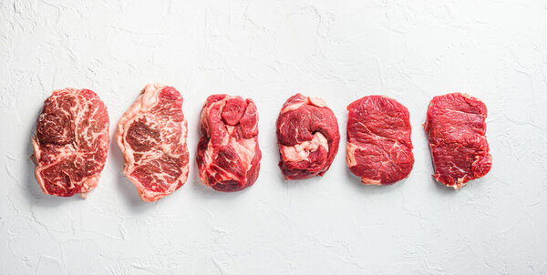 A set of different types of raw beef steaks:top blade, rump, chuck eye roll over white concrete background top view big size banner