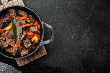 Tatlı dolma biberli et yahnisi ve defne yaprağı seti, dökme demir kızartma tavasında, siyah taş zemin üzerinde, üst görünüm düz, metin için kopyalama alanı ile