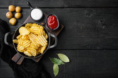 Ev yapımı patates cipsi seti, siyah ahşap arka planda, en üstteki düz yerde, metin için kopyalama alanı var.