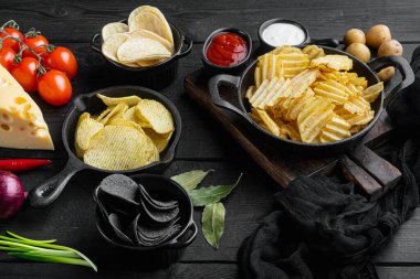 Farklı patates cipsi çeşitleri, siyah ahşap arka planda.