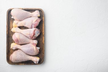 Çiğ tavuk bacakları seti, ahşap tepside, beyaz taş zemin üzerinde, üst görünüm düz, metin için kopyalama alanı ile