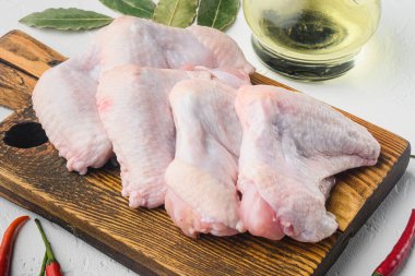 Çiğ tavuk kanatları, bitkiler, tahta kesme tahtası, beyaz arka plan