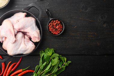 Çiğ et. Sebze ve baharatlı tavuk kanatları, kızgın demir tavada, siyah ahşap masa üzerinde, üst görünüm düz, metin alanı için kopyalama alanı