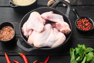 Baharatlı ve otlu taze çiğ tavuk kanatları, kızarmış demir tavada, siyah ahşap masada.