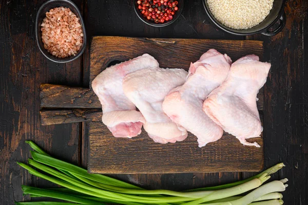 Chicken raw wings with rosemary , garlic , pepper and salt set, on wooden cutting board, on old dark  wooden table, top view flat lay