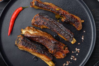 Domuz kaburgaları barbekü sosuyla ızgara ve bal setiyle karamelize edilmiş, tabakta, siyah ahşap masa zemininde, üst düz manzaralı