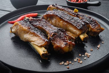 Barbekü domuz pirzolası, meyve aromalı, tabakta, siyah ahşap masa arkasında.