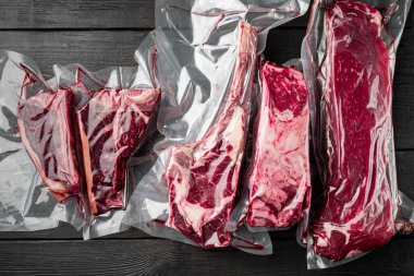 Plastik market paketi taze biftek seti, tomahawk, t kemik, kulüp bifteği, pirzola ve fileto kesimi, siyah ahşap masa arka planında, üst görünüm düz yatıyordu