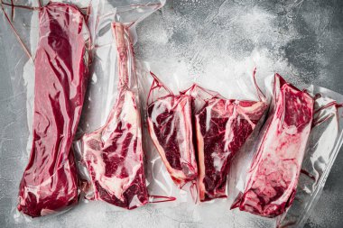 Plastik market paketi taze biftek seti, tomahawk, t kemik, kulüp bifteği, kaburga ve fileto kesikleri, gri taştan arka planda, üstten düz manzaralı.