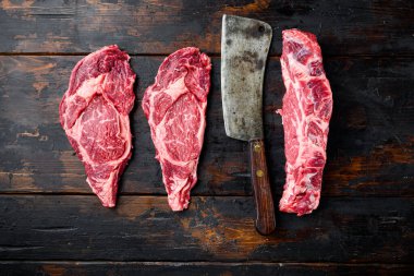 Pirzola bifteği taze çiğ et, mermer et, pirzola seti, eski siyah ahşap masa arka planı, üst görünüm düz yatıyordu