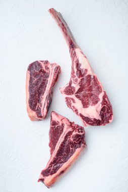 Kurumuş çiğ biftek et seti, tomahawk bifteği, kemik ya da biftek ve kulüp bifteği, beyaz taş arka planda, üst manzara düz yatıyordu.