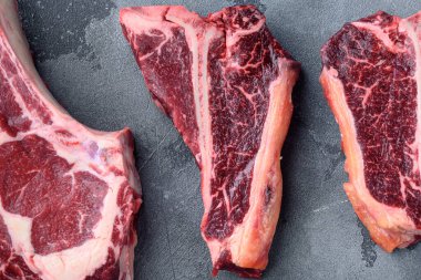 Kuru çiğ çiğ kemik veya biftek biftek biftek seti, gri taş arka planda, üst görünüm düz yatıyordu