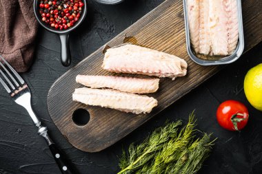 Konserve uskumru fileto, balık konserveleri ahşap kesme tahtasının üzerinde, siyah zemin üzerinde otlar ve malzemeler, üst görünüm düz yatıyordu.