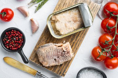 Konserve Wild Pink Somon seti, ahşap kesim tahtasında, beyaz arka planda otlar ve malzemelerle, üst manzara düz yatıyordu.