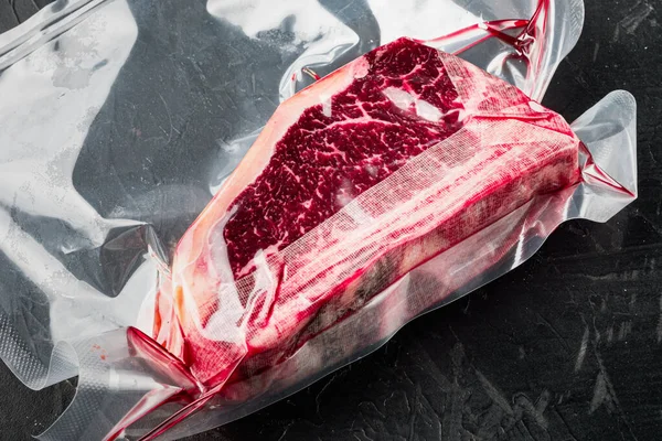 Fresh marbled meat black angus steak in vacuum plastic bag for sous vide set, on black stone background