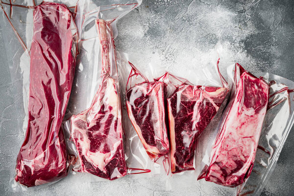 Plastic Market pack with fresh beef steak set, tomahawk, t bone, club steak, rib eye and tenderloin cuts, on gray stone background, top view flat lay