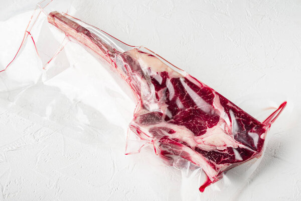 Raw fresh Dry aged raw tomahawk beef steak meat in plastic vacuum package set, on white stone  background, with copy space for text