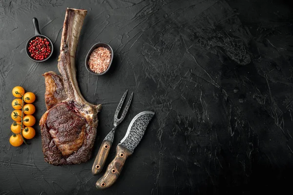 Grilled black angus beef tomahawk steak on bone set, on black stone background, top view flat lay, with copy space for text