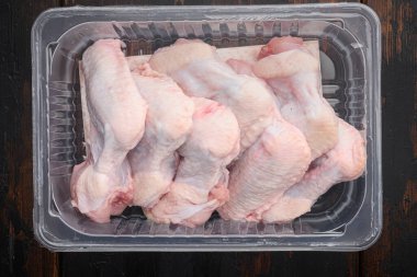 Taze tavuk kanatları plastik vakum paketine tükürür, eski, siyah ahşap masa zeminine, üst manzara düz