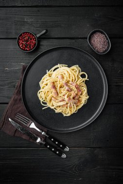 Carbonara makarnası. Pancetta 'lı spagetti, yumurta, parmesan peyniri seti, siyah ahşap arka planda, üst manzara düz.